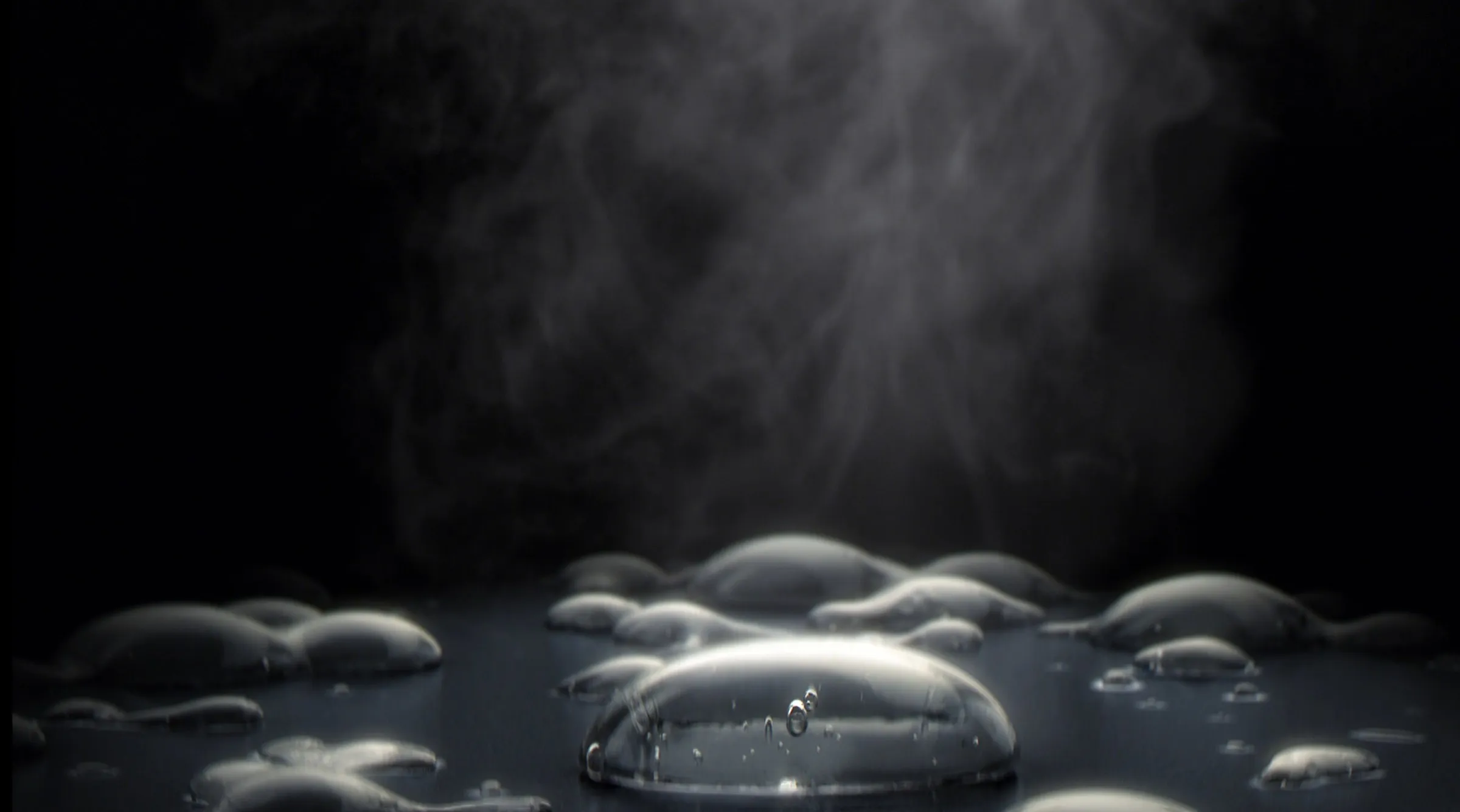 Nahaufnahme von Wassertropfen auf dunkler Fläche mit Dampf im Hintergrund