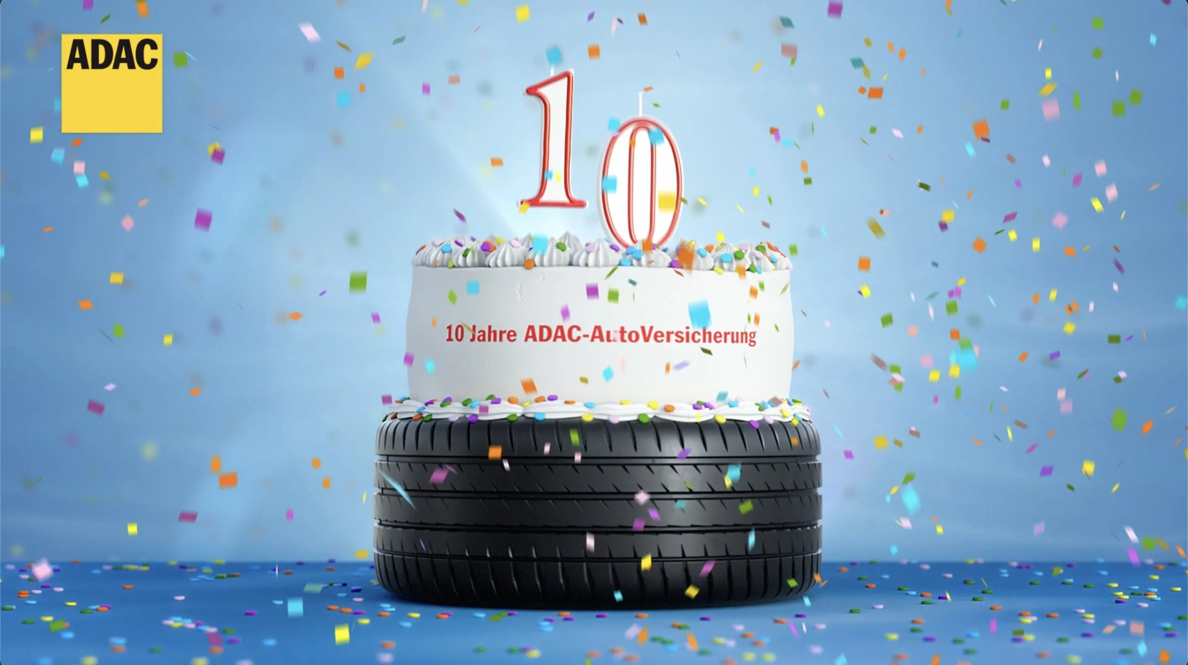 3D-Kuchen aus zwei Etagen, obere Etage aus Fondant mit brennenden Kerzen als Zahl 10, untere Etage aus einem Autoreifen, blauer Hintergrund mit Konfetti, ADAC-Logo oben links