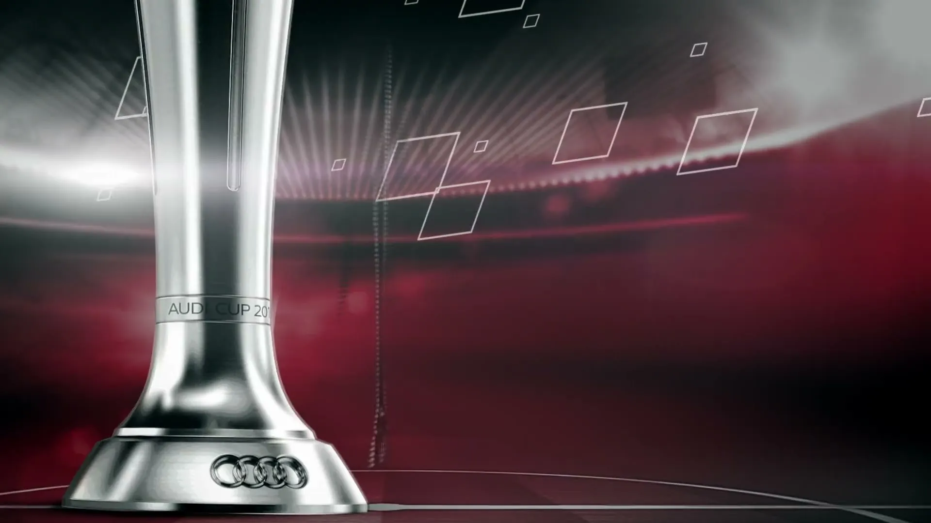 Silberner Pokal mit den vier Audi-Ringen an der Basis und eingravierter Schrift auf dem Schaft, davor computergrafische weiße Rautenformen, im Hintergrund ein rot-schwarz beleuchtetes Stadion