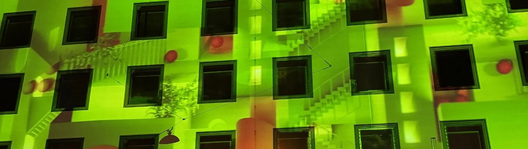 Fassadenprojektion in Grün mit roten Kugelakzenten auf einer Häuserfront, ein Treppenmotiv ist erkennbar
