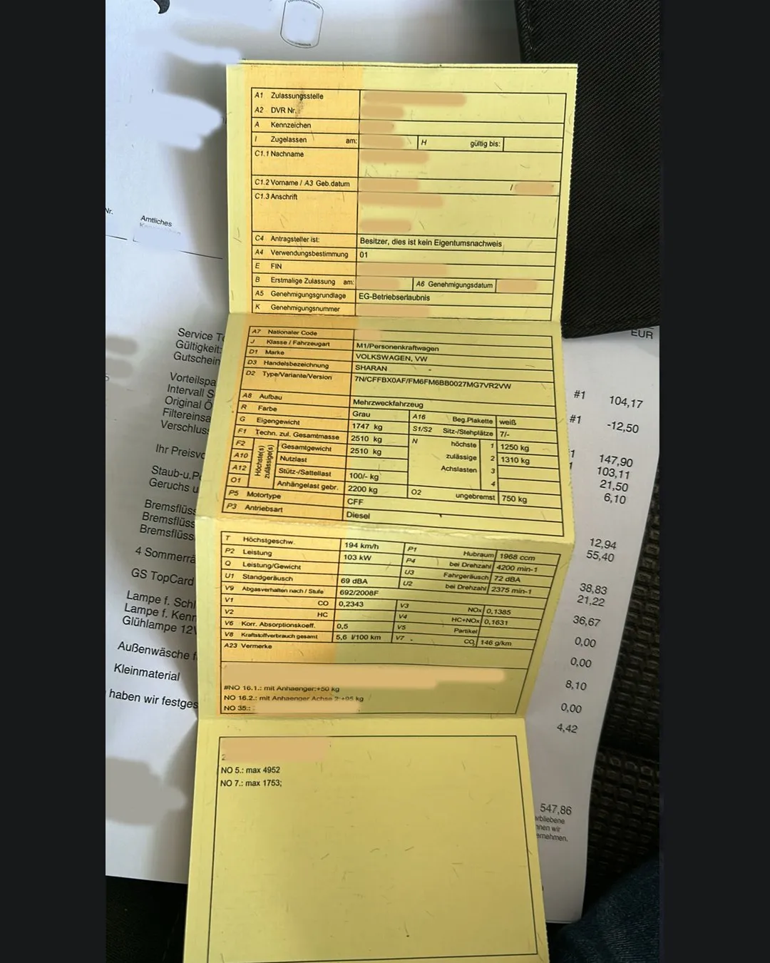 Ein aufgefalteter gelber Fahrzeugschein auf einer Werkstattrechnung, personenbezogene Felder wie Kennzeichen, Name, Anschrift und Fahrgestellnummer abgedeckt, sichtbar bleiben Marke, Typ und technische Daten des Fahrzeugs