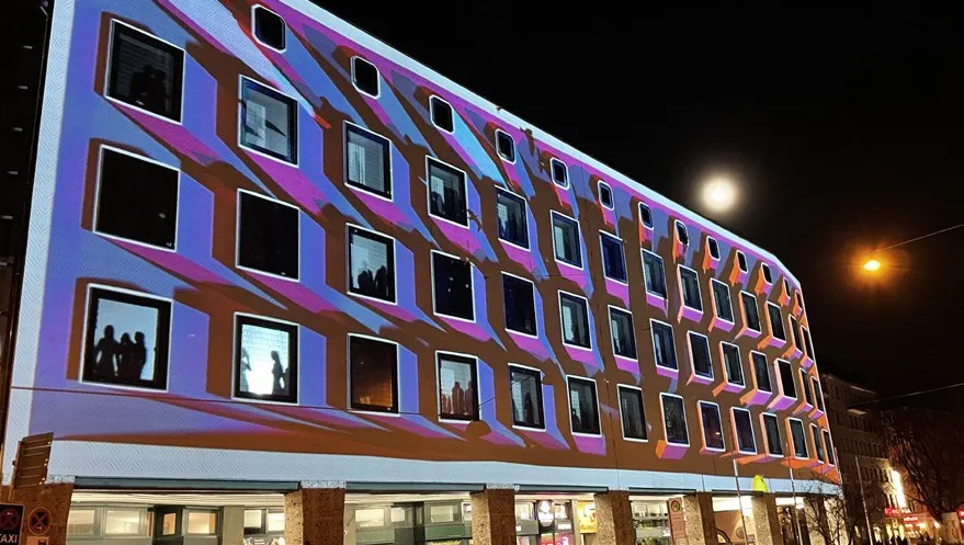 Fassadenprojektion mit lila-blauen Streifen und Formen auf einer Gebäudeecke bei Nacht, Mond im Hintergrund